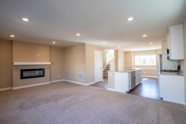 kitchen featuring white cabinets, stainless steel appliances, dark wood-type flooring, and an island with sink