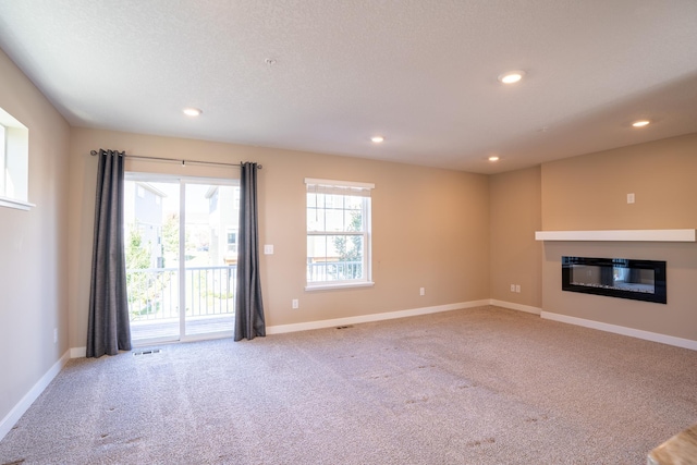 unfurnished living room with light carpet, a textured ceiling, and a healthy amount of sunlight