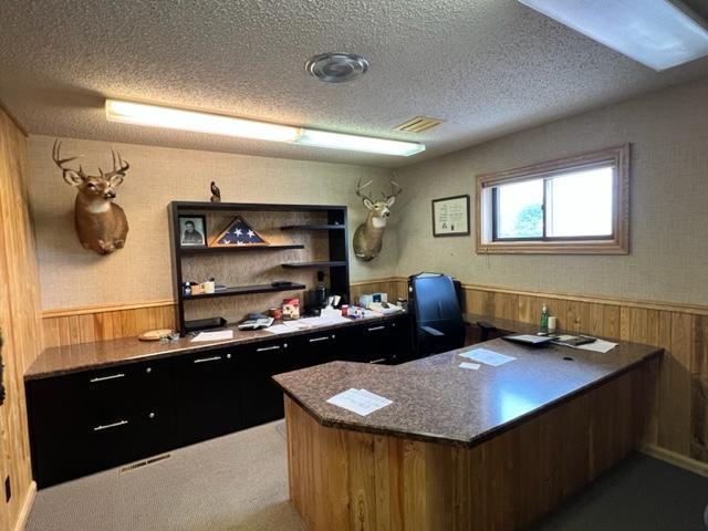 office area with dark colored carpet, a textured ceiling, and wood walls