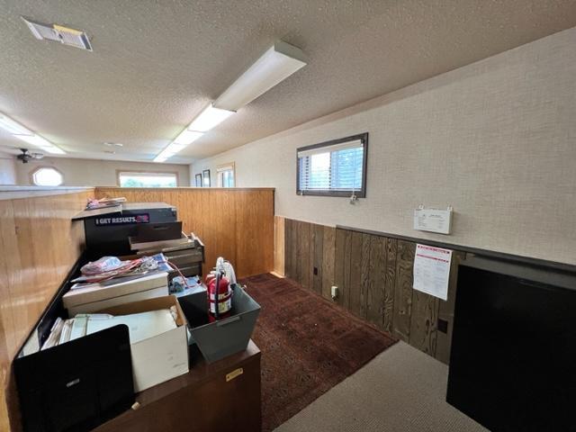 office with ceiling fan, a healthy amount of sunlight, wooden walls, and a textured ceiling