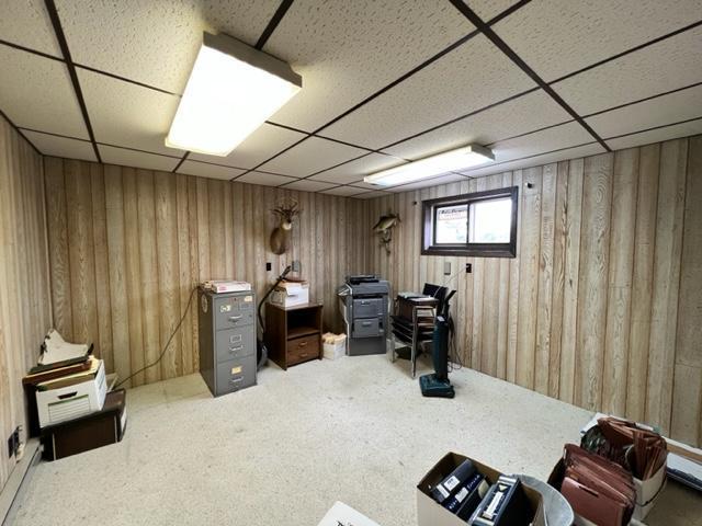 carpeted office with wood walls and a paneled ceiling