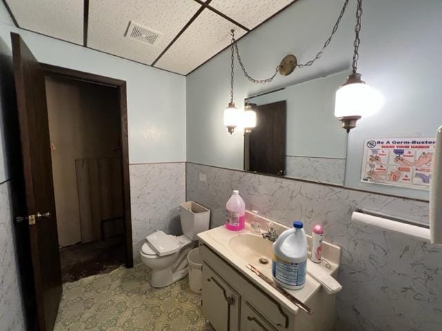 bathroom featuring tile patterned flooring, tile walls, a drop ceiling, toilet, and vanity