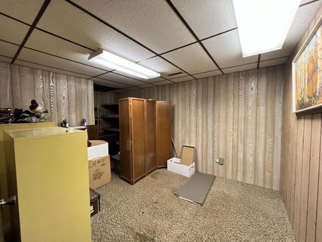 basement featuring a drop ceiling, carpet, and wood walls