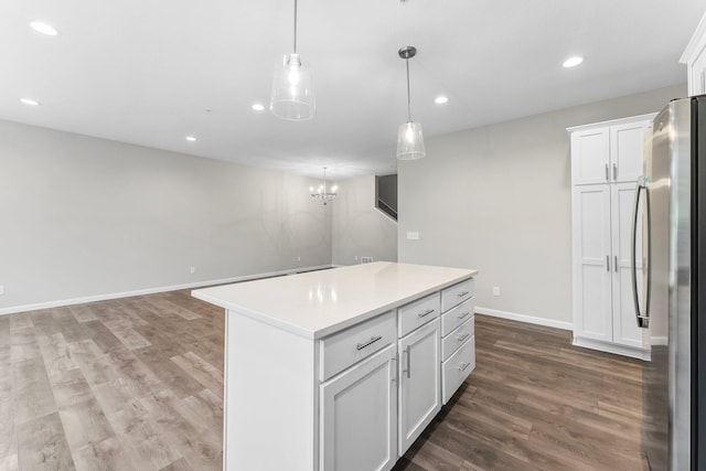 kitchen featuring decorative light fixtures, wood-type flooring, a center island, stainless steel refrigerator, and white cabinets