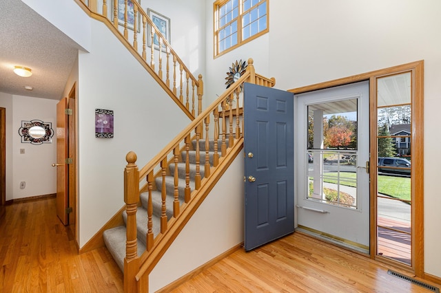 foyer entrance with baseboards, visible vents, a towering ceiling, wood finished floors, and a textured ceiling