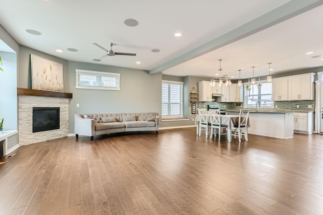 unfurnished living room with sink, a stone fireplace, hardwood / wood-style floors, and ceiling fan