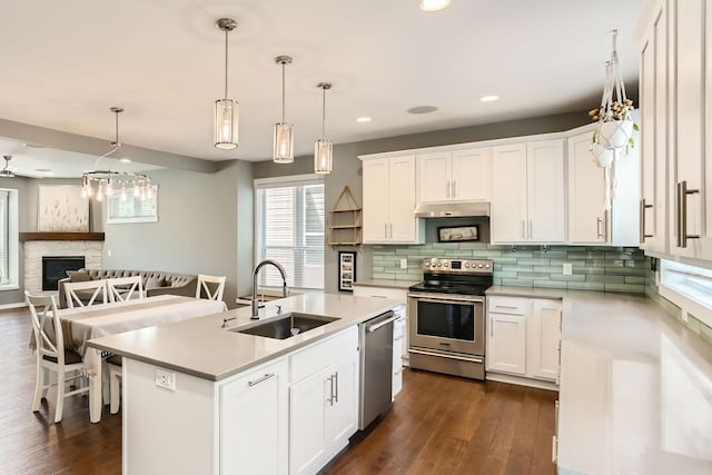 kitchen featuring dark hardwood / wood-style flooring, an island with sink, stainless steel appliances, a stone fireplace, and sink