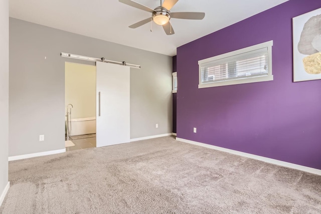 carpeted empty room with ceiling fan and a barn door