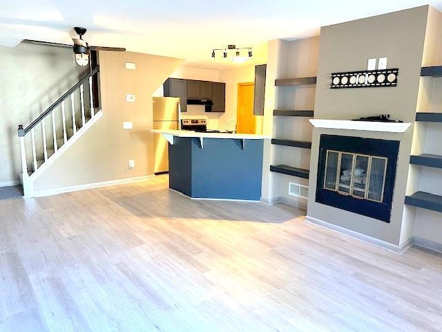 kitchen with kitchen peninsula, stainless steel refrigerator, ceiling fan, and light hardwood / wood-style floors