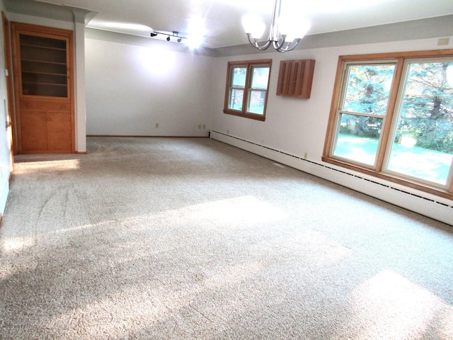 carpeted empty room featuring a baseboard radiator, a chandelier, a wall mounted AC, and rail lighting