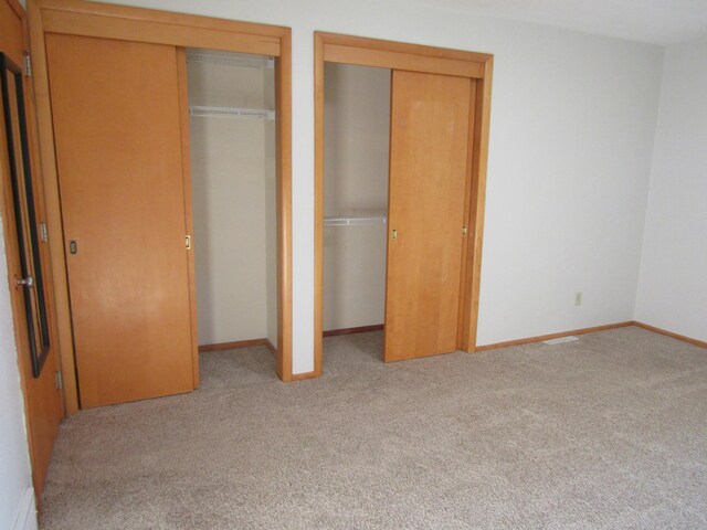 unfurnished bedroom featuring two closets and light carpet