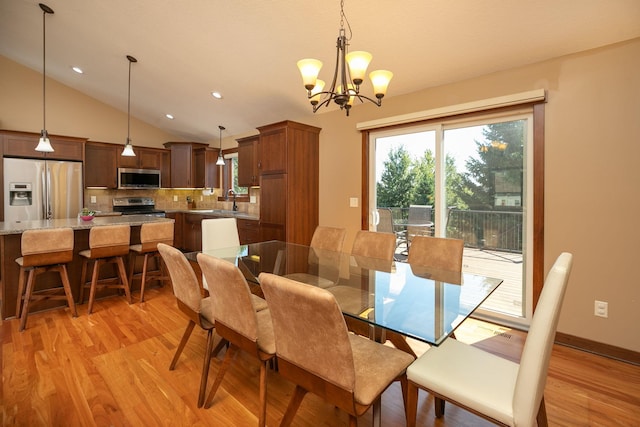 dining room with light hardwood / wood-style floors, vaulted ceiling, an inviting chandelier, and sink