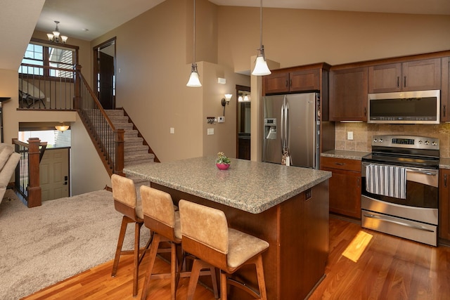 kitchen featuring pendant lighting, lofted ceiling, a kitchen breakfast bar, appliances with stainless steel finishes, and hardwood / wood-style floors