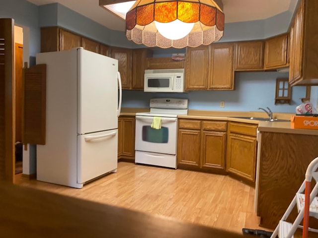 kitchen featuring hanging light fixtures, sink, white appliances, and light wood-type flooring