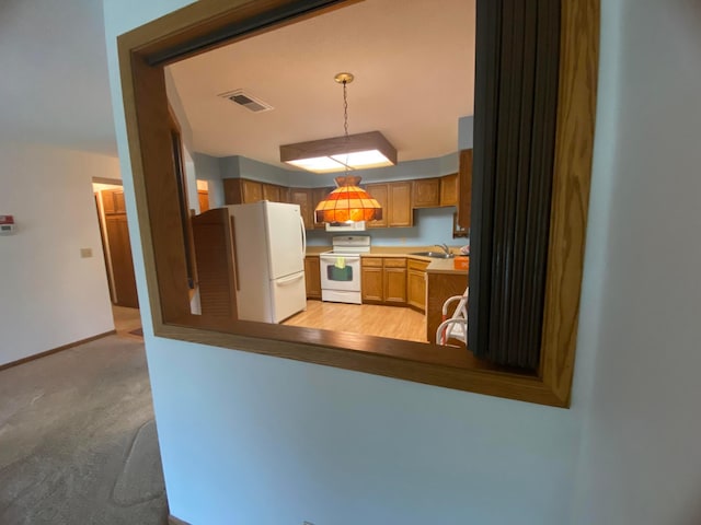 kitchen featuring hanging light fixtures, white appliances, sink, light colored carpet, and kitchen peninsula