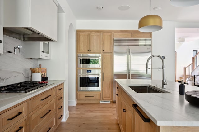 kitchen featuring light wood-type flooring, stainless steel appliances, decorative backsplash, decorative light fixtures, and sink