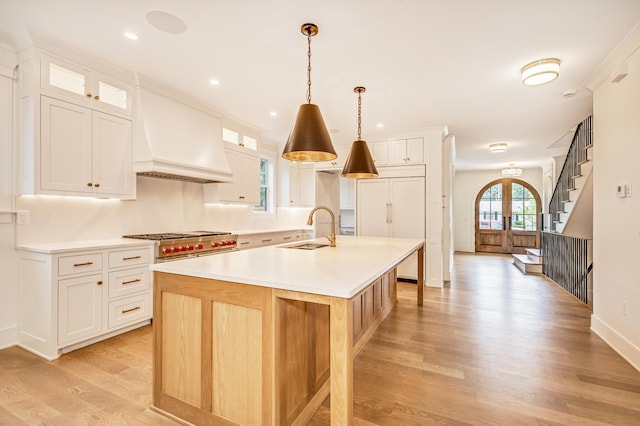 kitchen featuring light hardwood / wood-style floors, white cabinetry, custom exhaust hood, and an island with sink