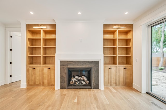 unfurnished living room with light hardwood / wood-style floors, built in shelves, and a high end fireplace