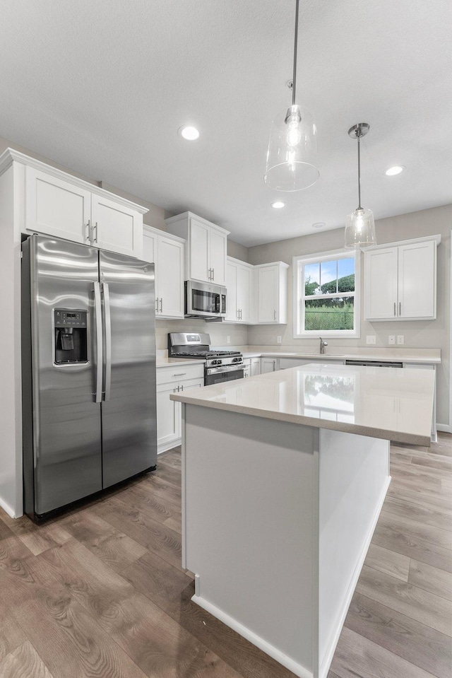 kitchen featuring hardwood / wood-style floors, pendant lighting, stainless steel appliances, and white cabinets