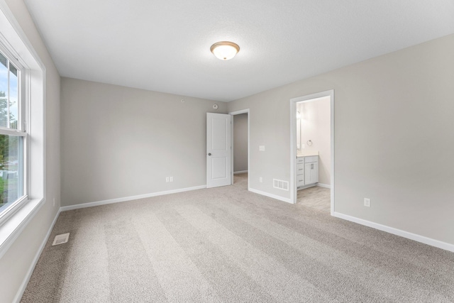 unfurnished bedroom with ensuite bathroom and light colored carpet