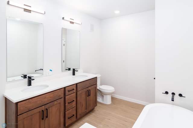 bathroom with a washtub, toilet, vanity, and hardwood / wood-style floors