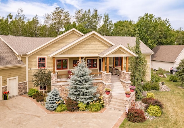 craftsman-style home with a porch, a shingled roof, and stone siding