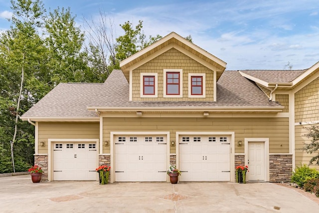 craftsman-style home with stone siding, an attached garage, driveway, and roof with shingles