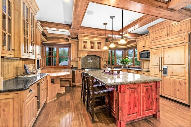 kitchen featuring dark wood-style flooring, built in appliances, a kitchen island with sink, and beamed ceiling
