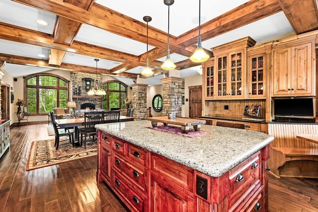 kitchen featuring a stone fireplace, open floor plan, ornate columns, dark wood-style floors, and coffered ceiling