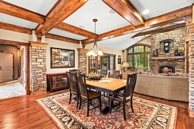 dining room featuring vaulted ceiling with beams, a fireplace, ornate columns, and wood finished floors