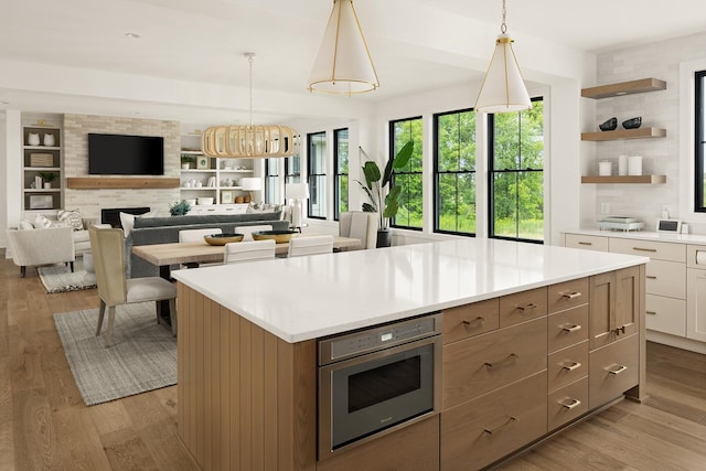 kitchen featuring stainless steel oven, white cabinets, a kitchen island, light hardwood / wood-style floors, and pendant lighting