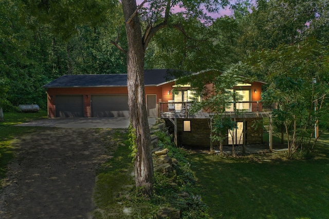 view of front facade with a garage, concrete driveway, a forest view, a deck, and a yard