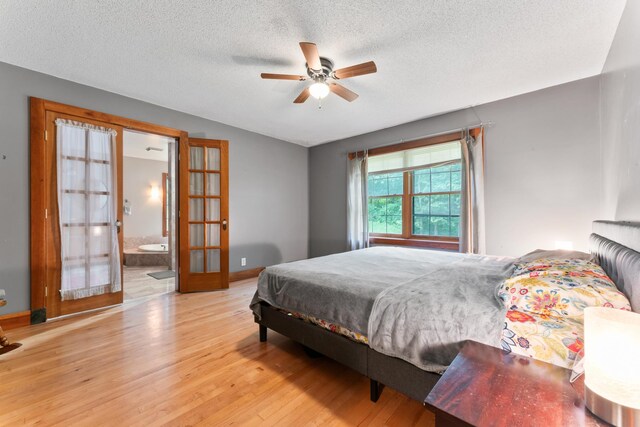 bedroom featuring french doors, a textured ceiling, light hardwood / wood-style floors, ceiling fan, and connected bathroom