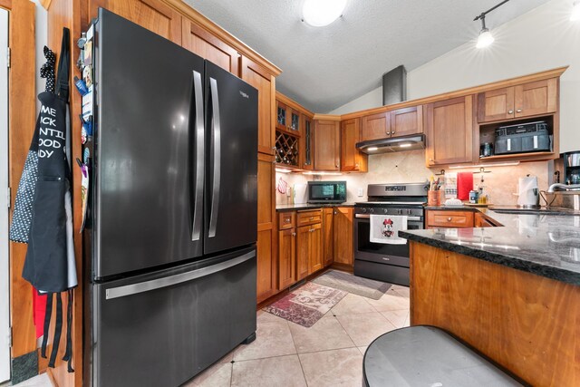 kitchen featuring vaulted ceiling, dark stone countertops, stainless steel range oven, refrigerator, and sink