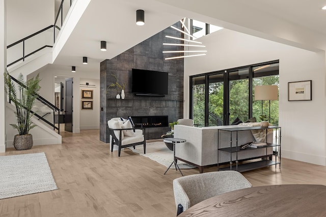 living room with tile walls, light wood-type flooring, an inviting chandelier, a tile fireplace, and a towering ceiling