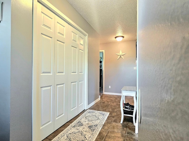 hallway with a textured ceiling and dark tile patterned flooring