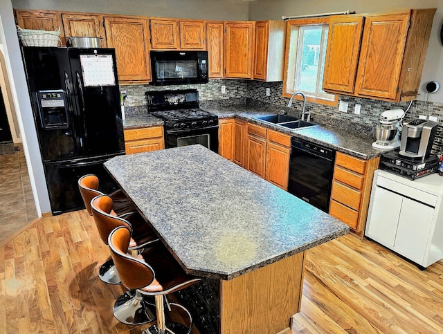 kitchen with a breakfast bar, black appliances, light hardwood / wood-style floors, and sink