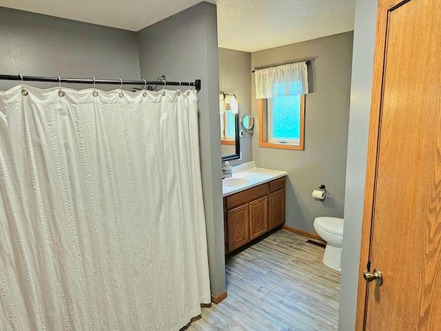 bathroom with a textured ceiling, walk in shower, hardwood / wood-style floors, vanity, and toilet