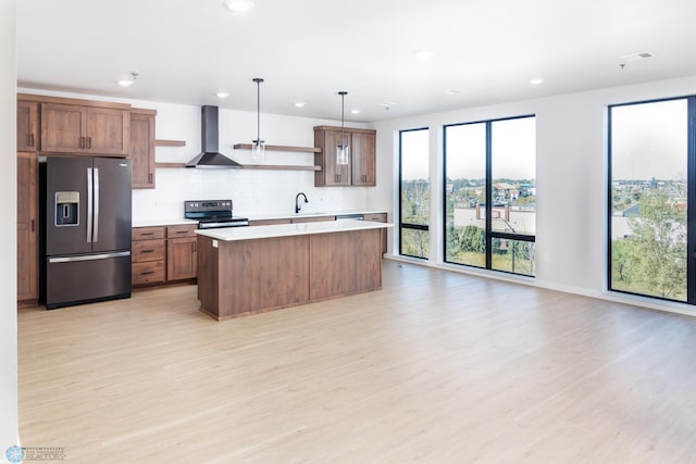 kitchen with light hardwood / wood-style floors, sink, wall chimney range hood, stainless steel appliances, and decorative light fixtures