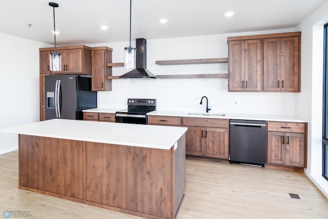 kitchen featuring hanging light fixtures, sink, wall chimney exhaust hood, stainless steel appliances, and light wood-type flooring