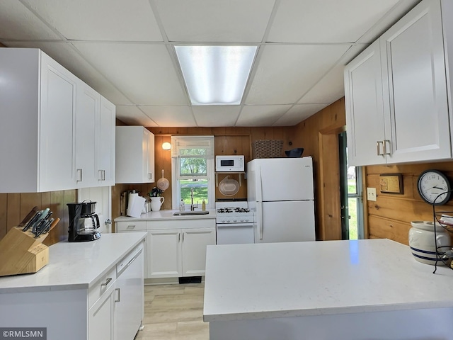 kitchen with white cabinets, white appliances, wooden walls, a paneled ceiling, and light hardwood / wood-style flooring