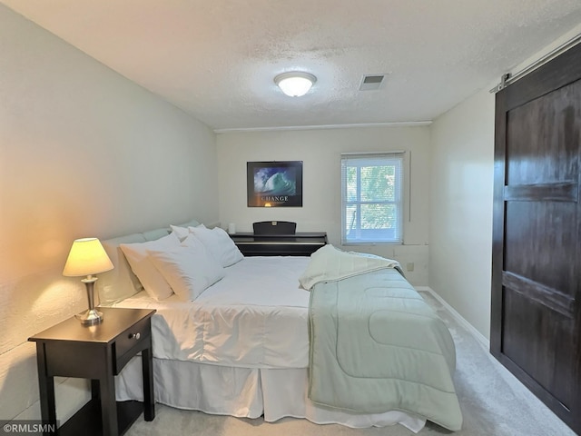 bedroom featuring light colored carpet, a textured ceiling, and a barn door