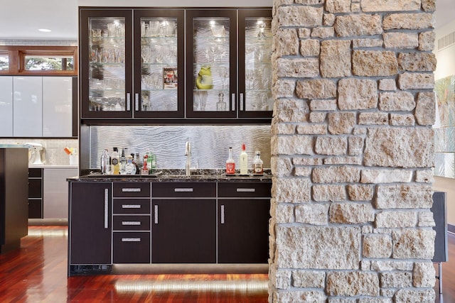 bar featuring dark stone counters, decorative backsplash, and hardwood / wood-style flooring