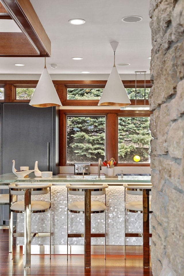 bar with hanging light fixtures, stainless steel refrigerator, dark hardwood / wood-style flooring, and light stone countertops