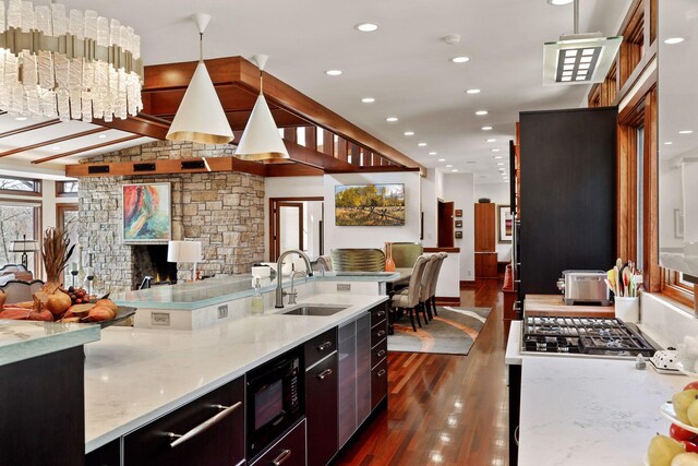 kitchen featuring dark wood-type flooring, light stone counters, a stone fireplace, black microwave, and sink