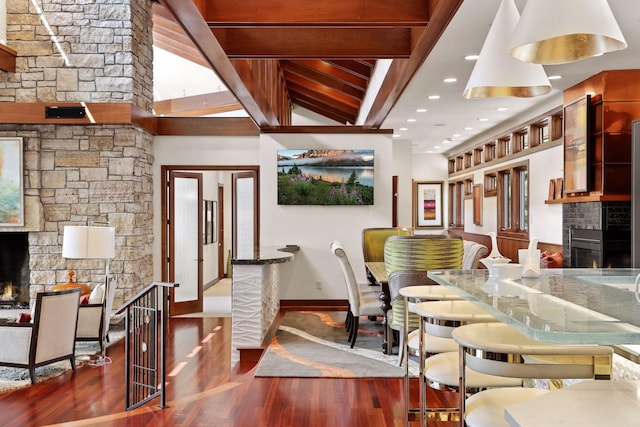 dining room featuring vaulted ceiling with beams, a stone fireplace, and dark hardwood / wood-style flooring