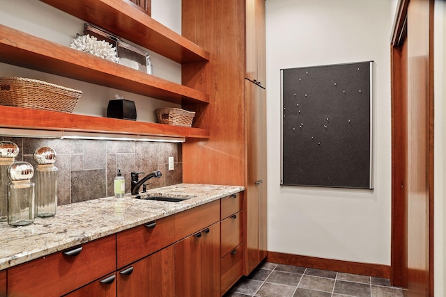 bar with dark tile patterned floors, sink, light stone counters, and tasteful backsplash