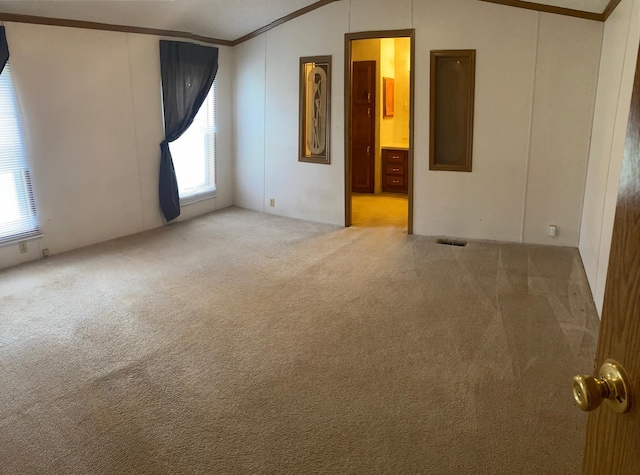 empty room featuring crown molding, vaulted ceiling, a healthy amount of sunlight, and carpet flooring