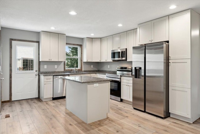 kitchen with stone counters, appliances with stainless steel finishes, a center island, and light wood-type flooring