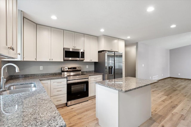 kitchen featuring sink, white cabinets, a center island, stainless steel appliances, and light stone countertops